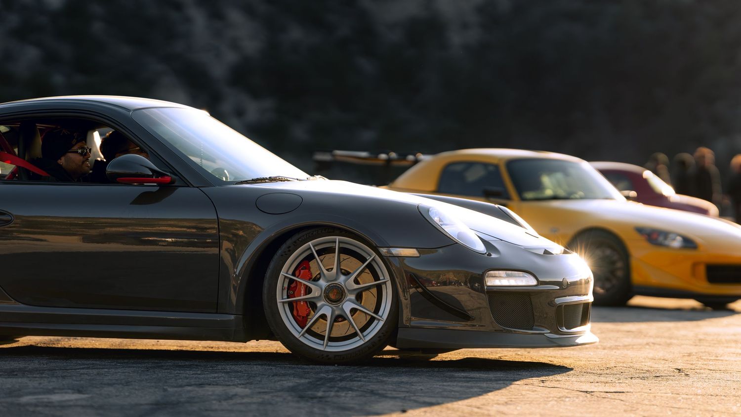 Row of luxury sports cars parked against dramatic sunset backdrop.