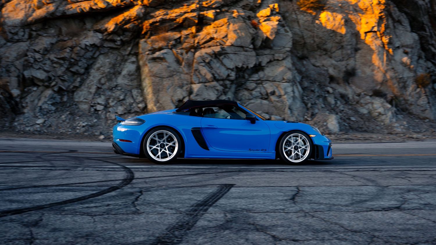 Bright blue sports car parked against rocky mountain backdrop during sunset.