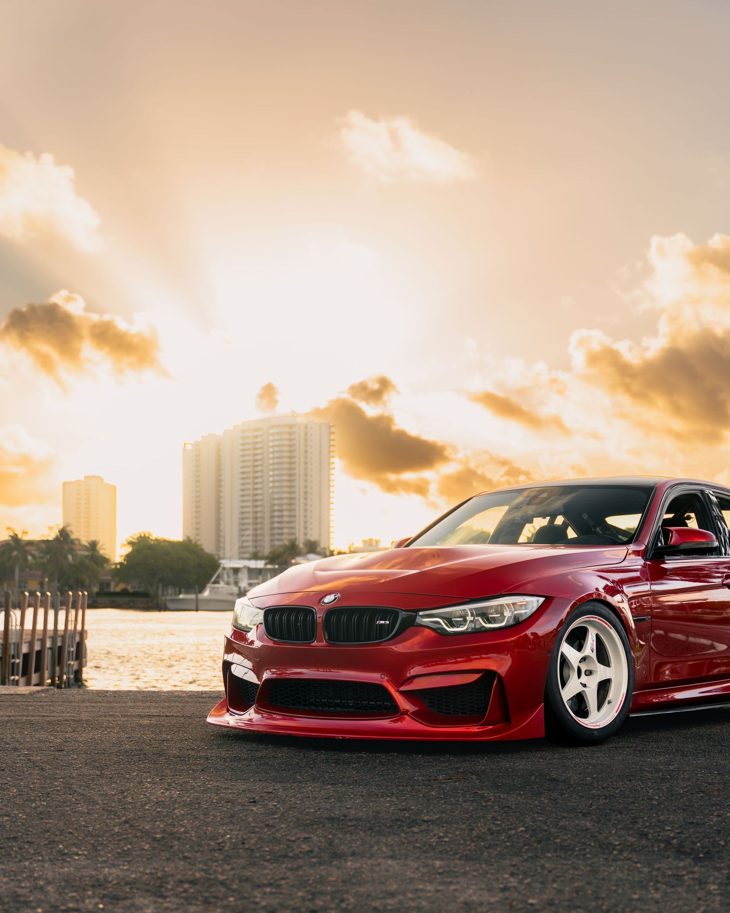 Red BMW M3 sports car with white wheels parked at sunset, featuring aggressive body kit and lowered stance.