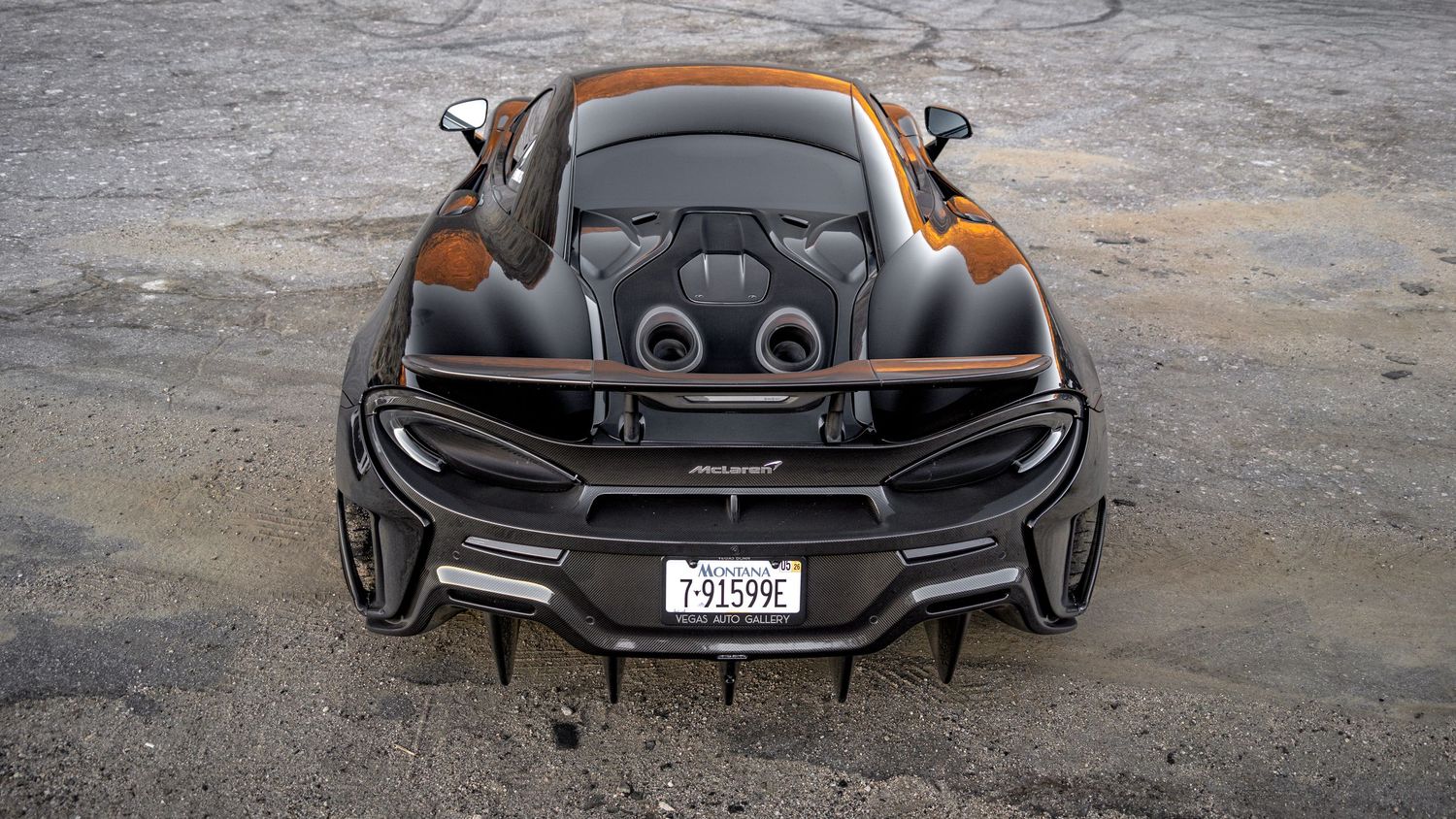 Panoramic rear view of a sleek black McLaren supercar on concrete surface.