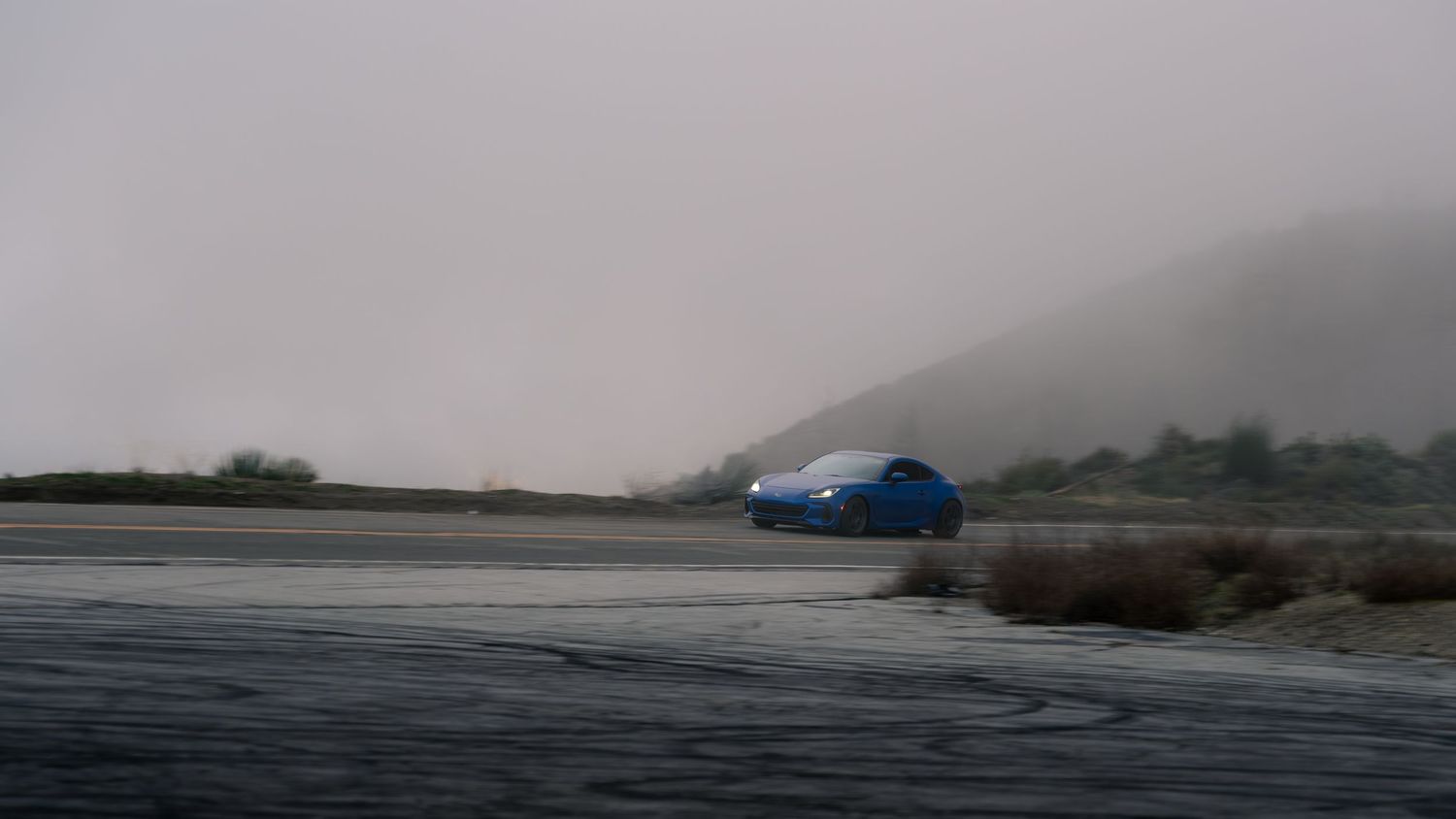 Misty coastal road with luxury vehicles in the distance.