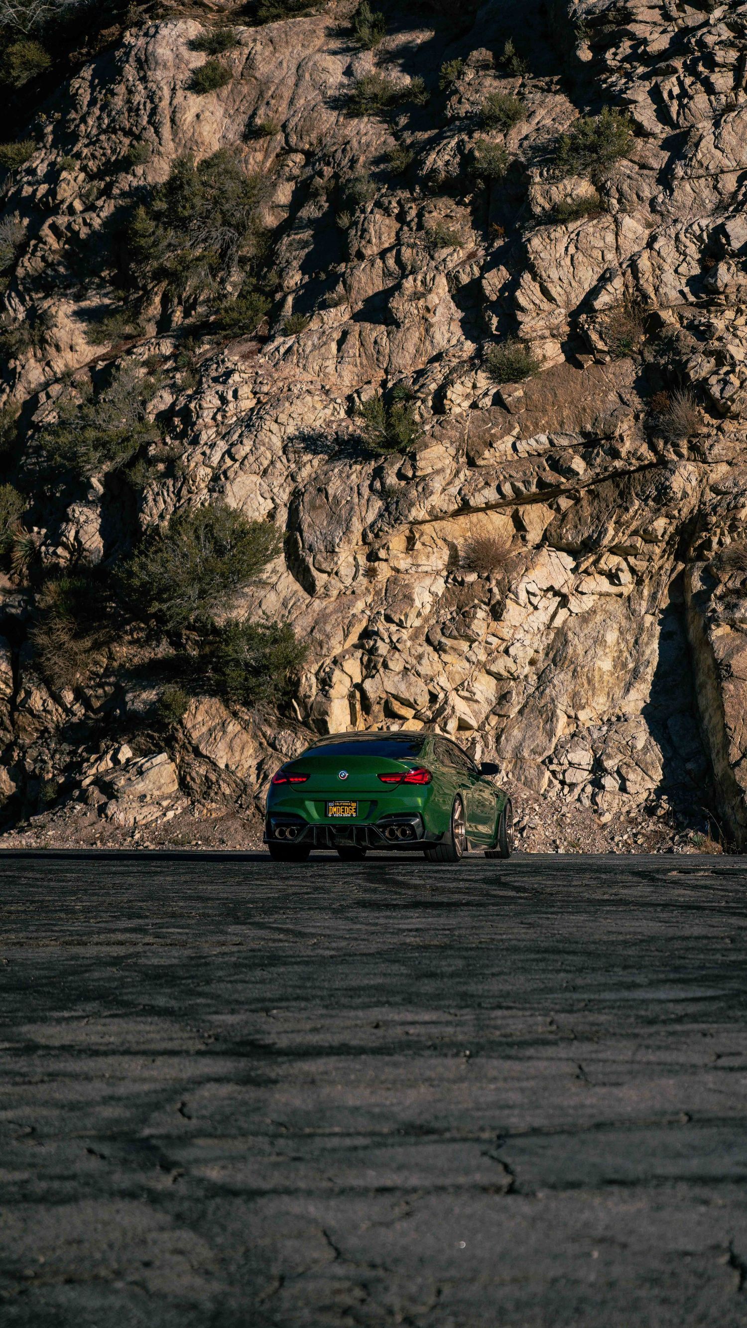 Sports car silhouetted against dramatic rocky cliff face in natural lighting.