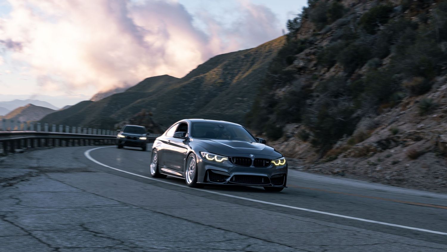 Performance cars taking turns on a mountainous coastal road.