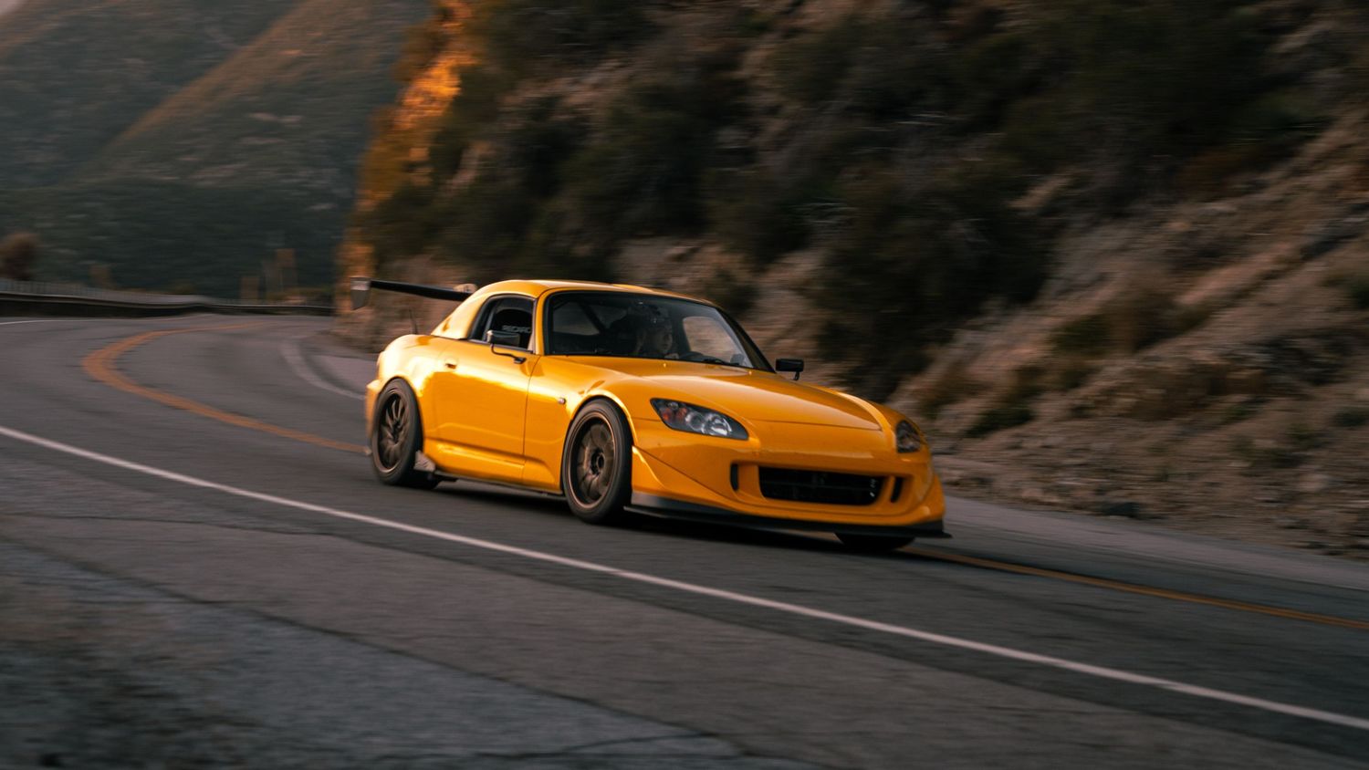 Yellow performance car taking a sharp turn on a mountain pass.