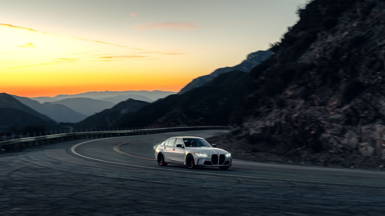 BMW sports car driving on winding mountain road during golden hour sunset.