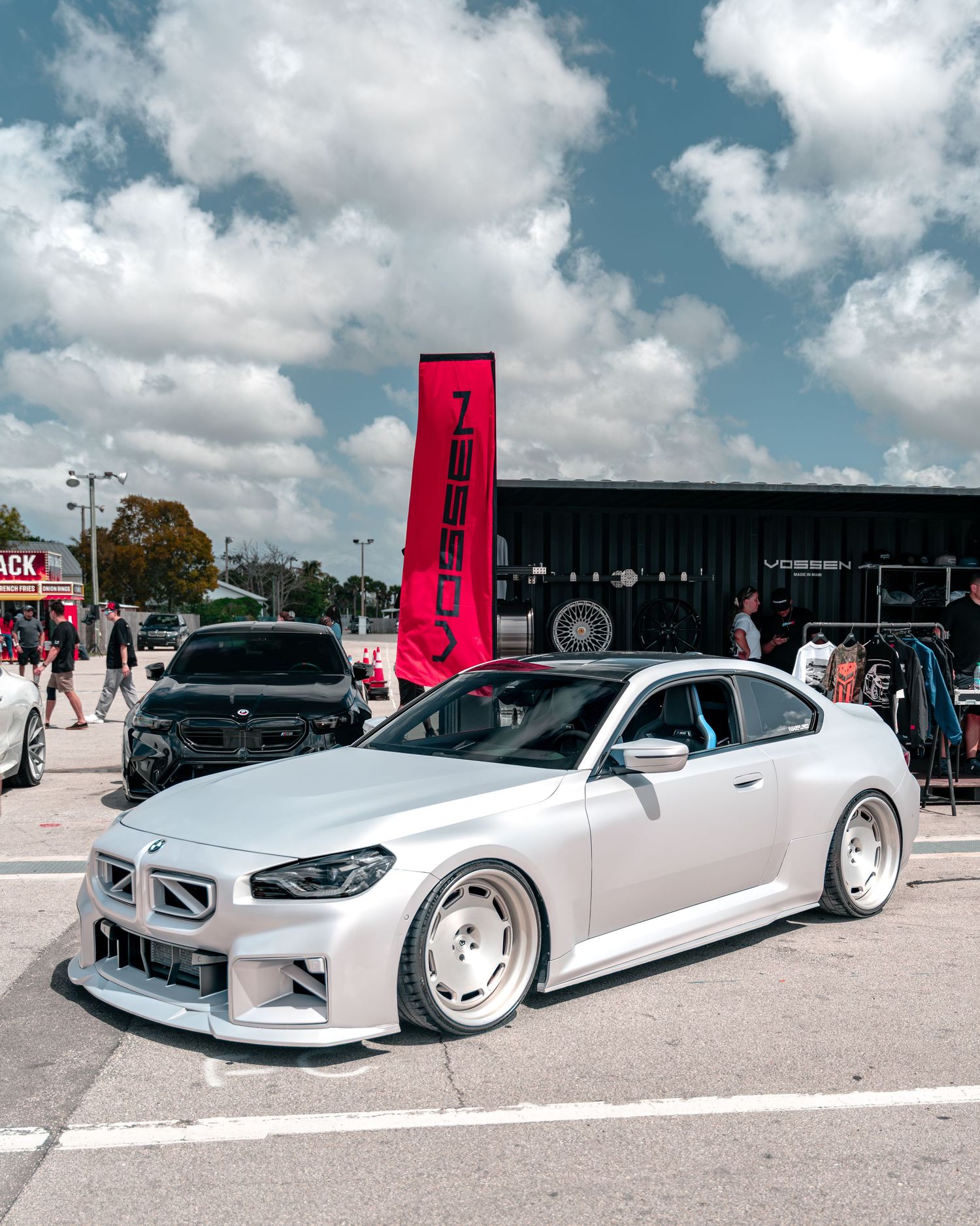 Modified silver sports car with wide body kit at an outdoor car show, featuring lowered stance and custom wheels.