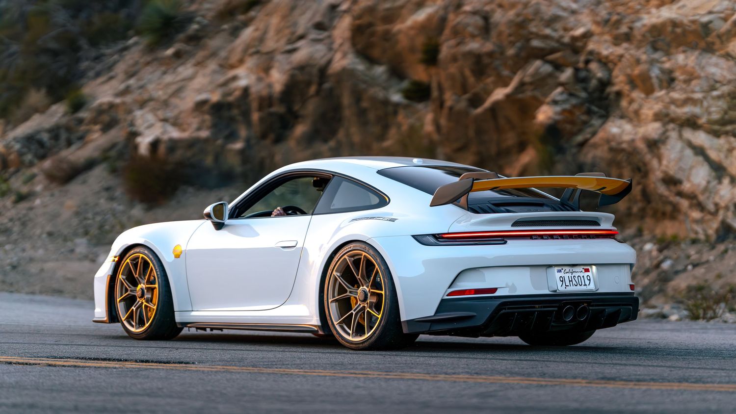 White Porsche sports cars driving on a winding mountain road with scenic views.