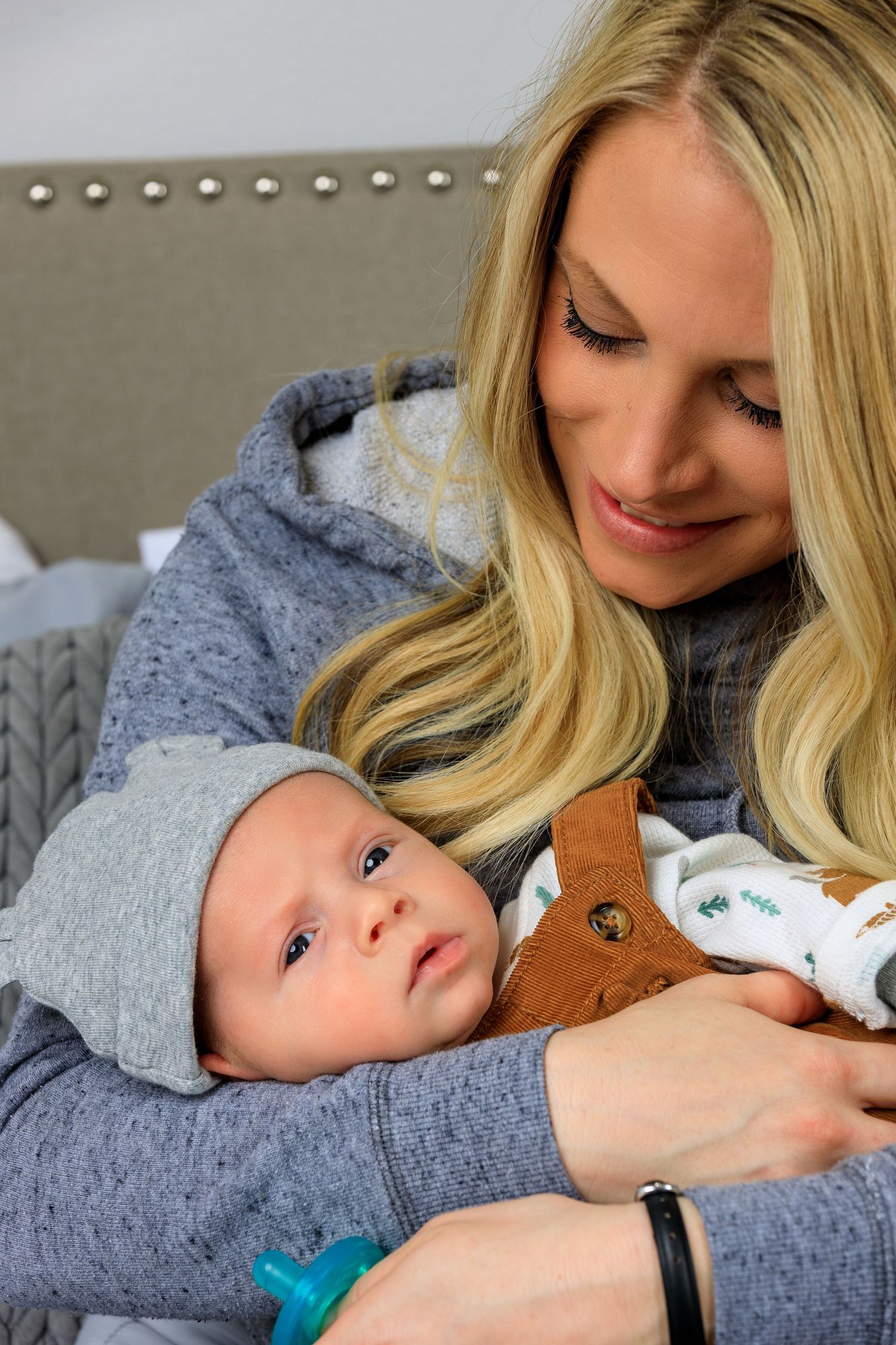 A tender moment between parent and baby lying together on a grey couch.