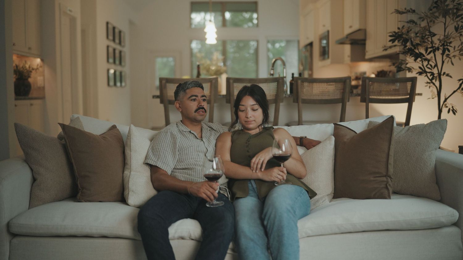 Two people sit comfortably on a gray couch while watching TV in a modern living room with natural lighting.