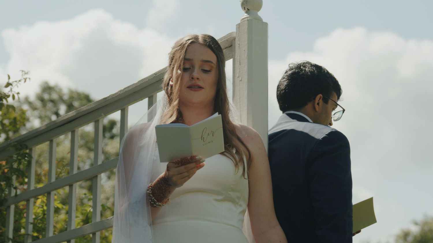 Outdoor wedding ceremony at a white gazebo under cloudy summer skies.
