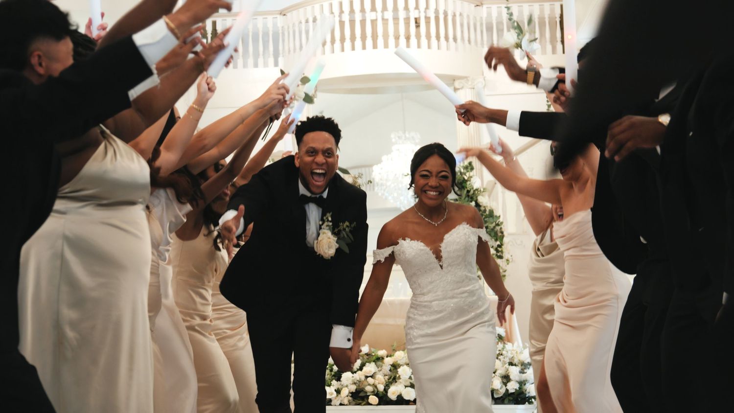 Joyful wedding party celebrates as newlyweds walk through a tunnel of raised arms at outdoor ceremony.