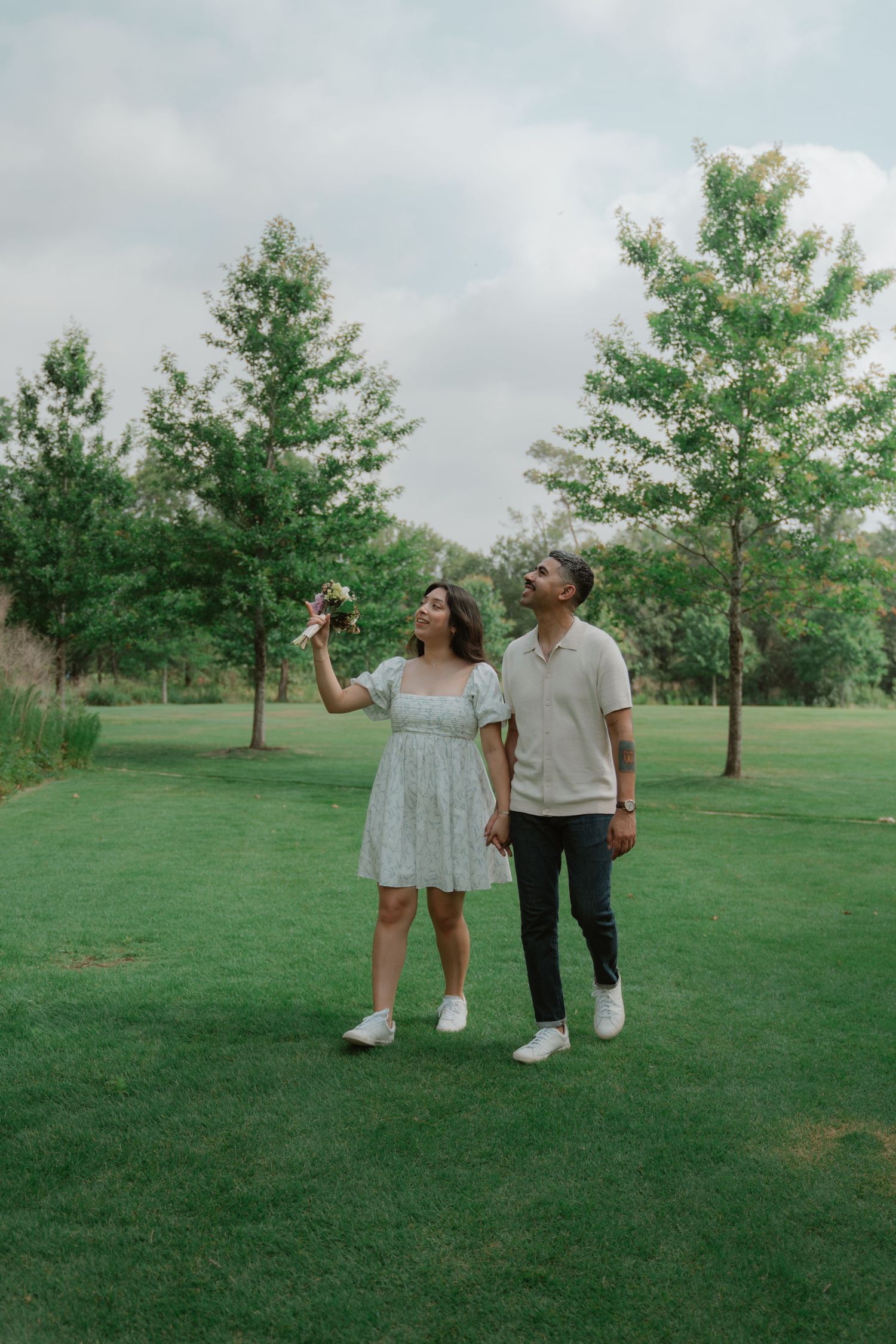 A couple walking together on a green lawn holding champagne glasses.