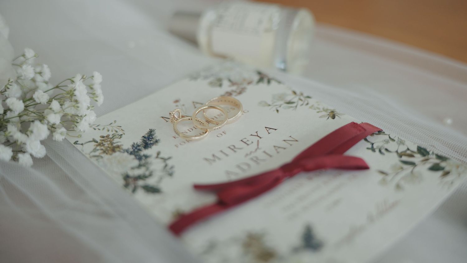 A delicate white floral wedding invitation suite with burgundy ribbon and elegant calligraphy details.