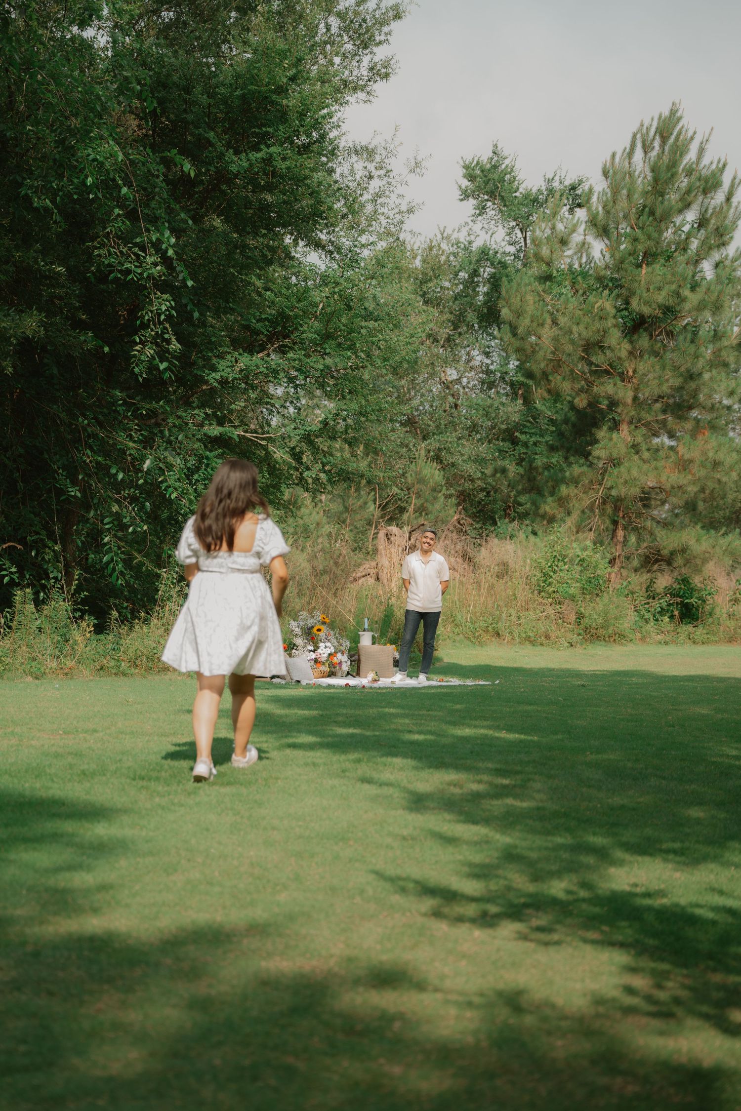 A romantic picnic setup on a grassy lawn with people in white outfits.