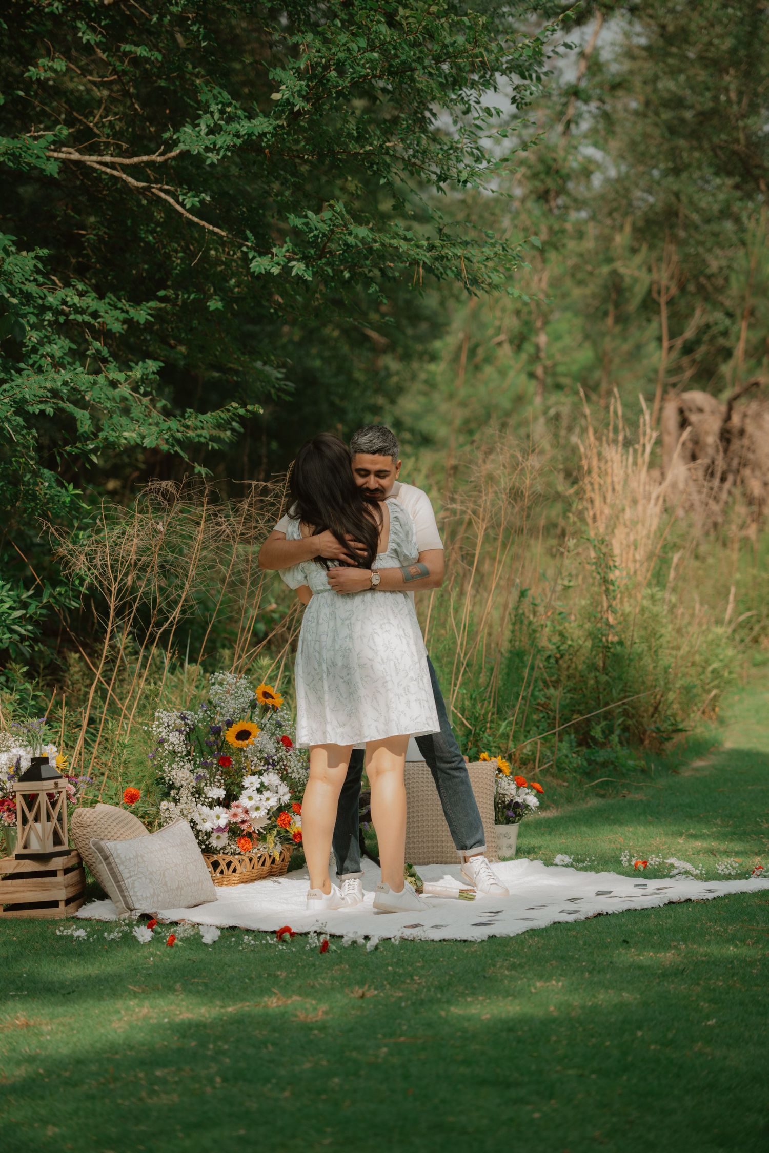 An intimate outdoor picnic scene with flowers and decorative elements on a white blanket.