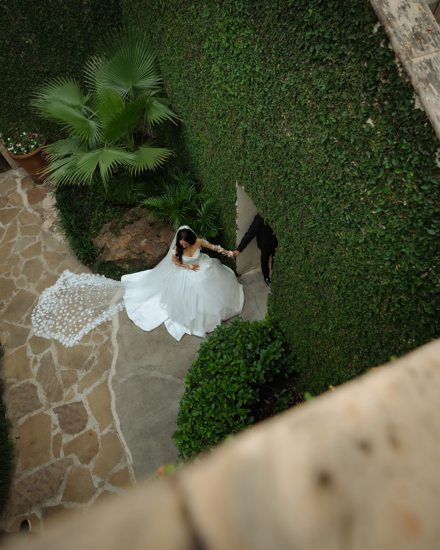 Bird's eye view of bride in white dress walking along stone pathway in garden.
