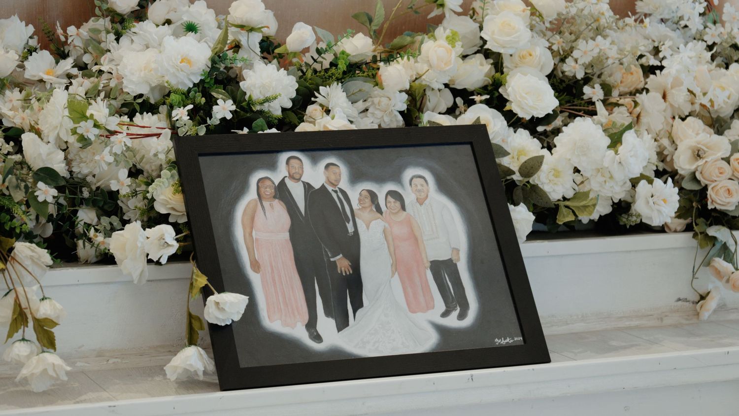 Wedding decor featuring white floral arrangements and framed photographs on display.