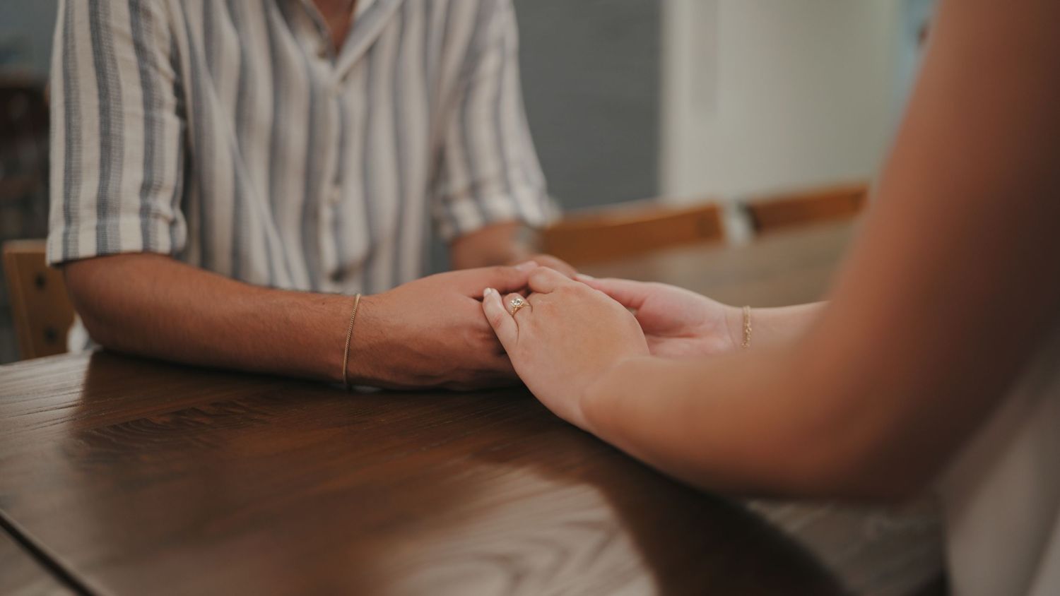 Close-up shot of hands holding each other across a wooden table surface.