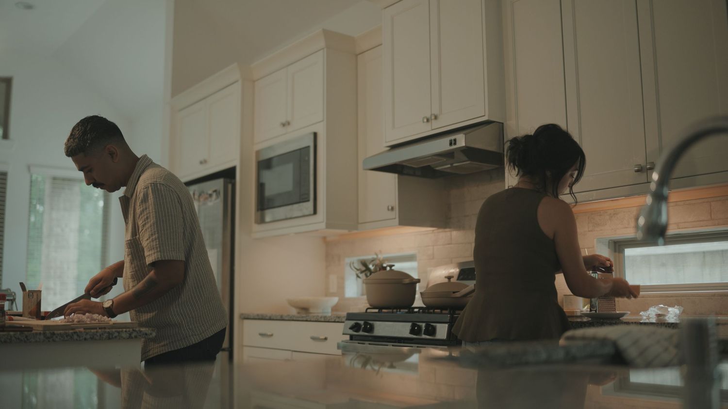 Two people prepare food together in a modern white kitchen with under-cabinet lighting.