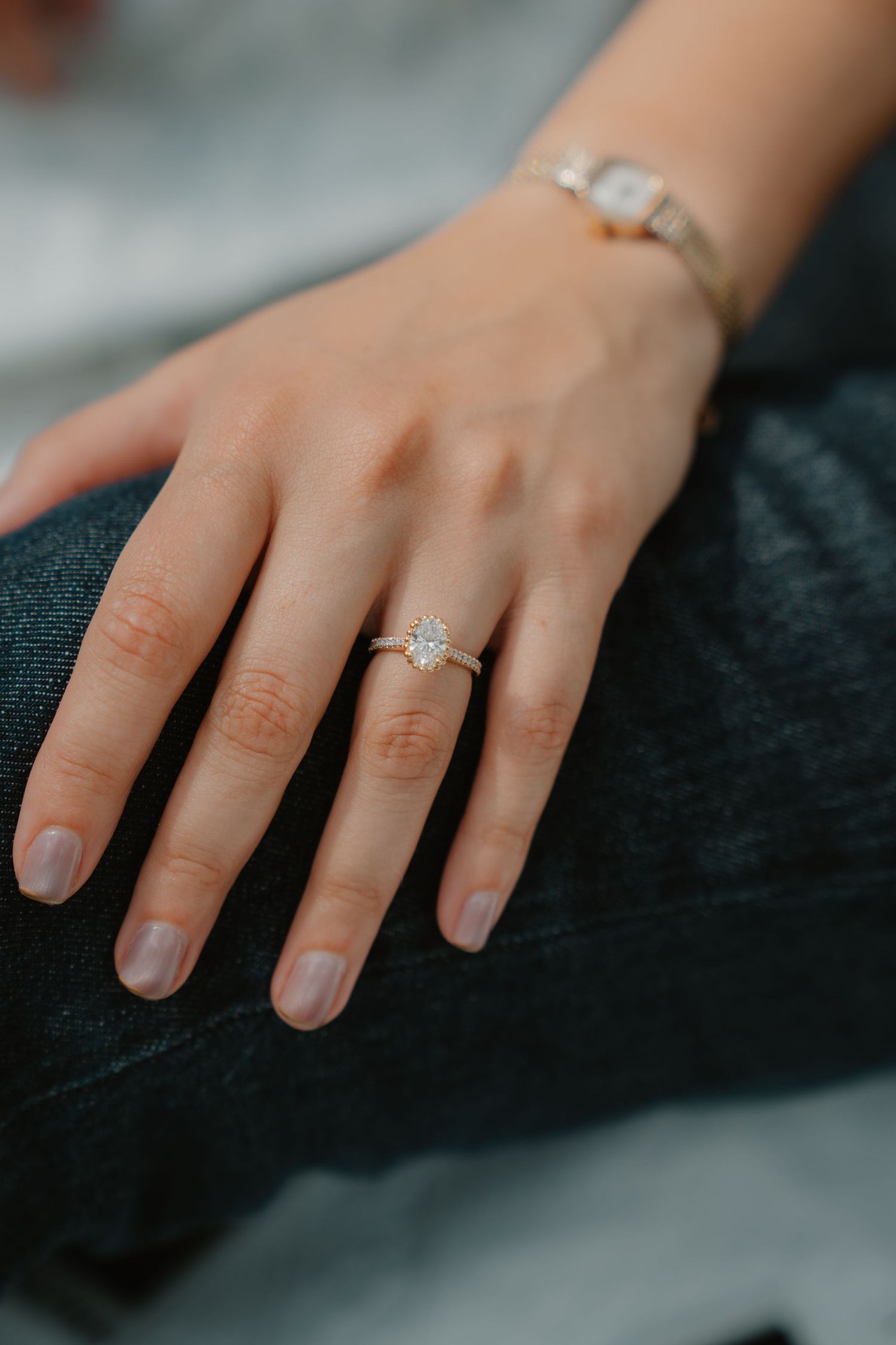 A close-up of a hand wearing an engagement ring against a dark background.