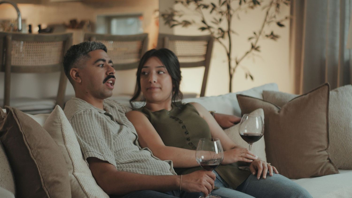 A family relaxes together on a brown couch in a warmly lit living room.