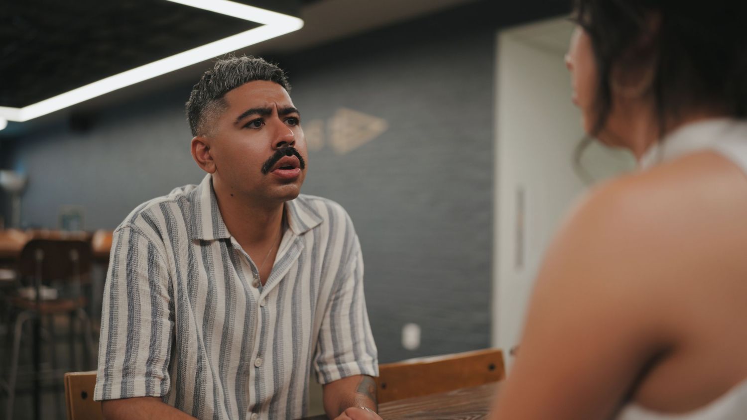Two people having an animated conversation in a dimly lit indoor setting.
