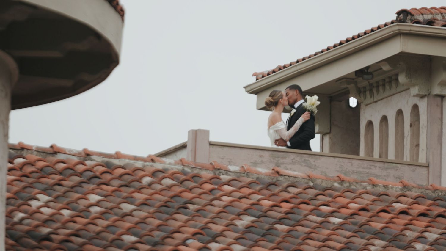 A Spanish-style terracotta tile roof with curved edges and ornate architectural details against a cloudy sky.