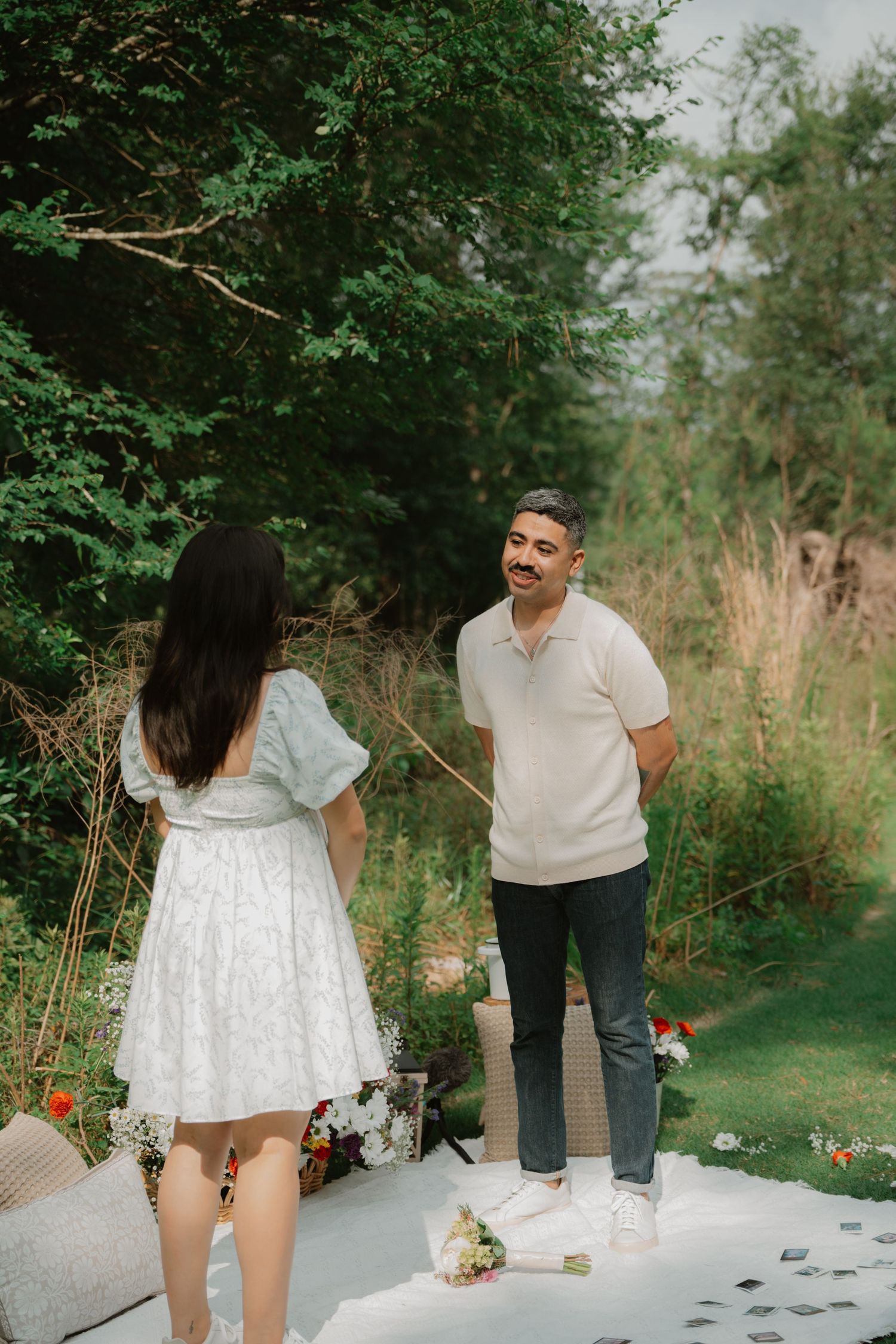 A couple sharing a romantic moment on a white blanket with picnic decorations.