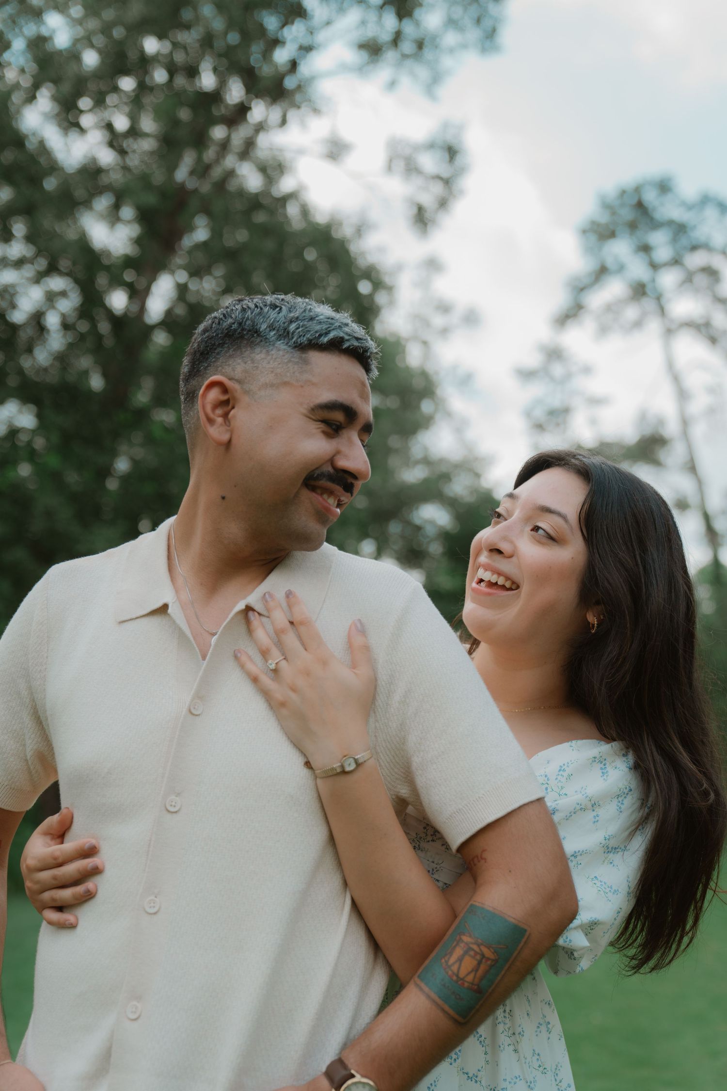 A couple shares a joyful moment together outdoors in a natural setting with soft lighting and greenery in the background.