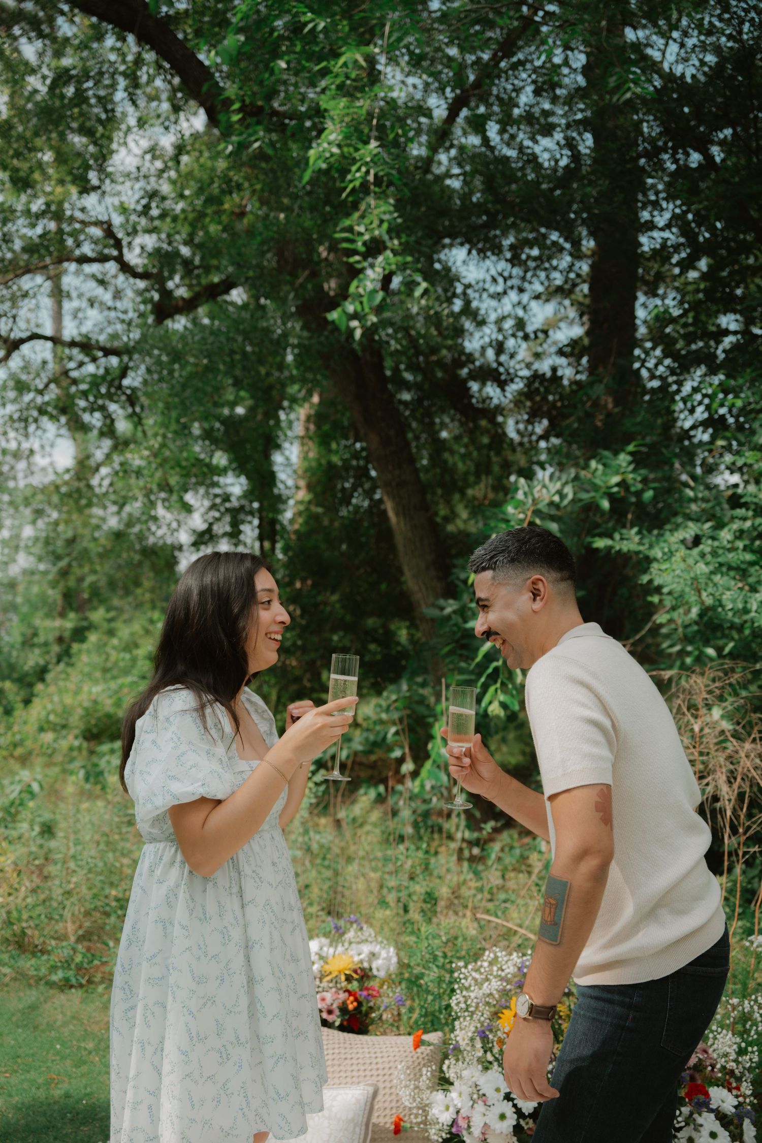 A couple sharing champagne and laughing during an outdoor picnic celebration.