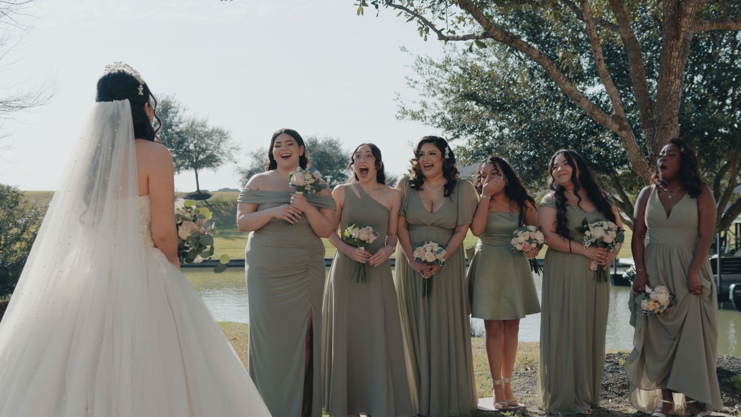Bridesmaids in sage green dresses gather outdoors during a wedding ceremony.
