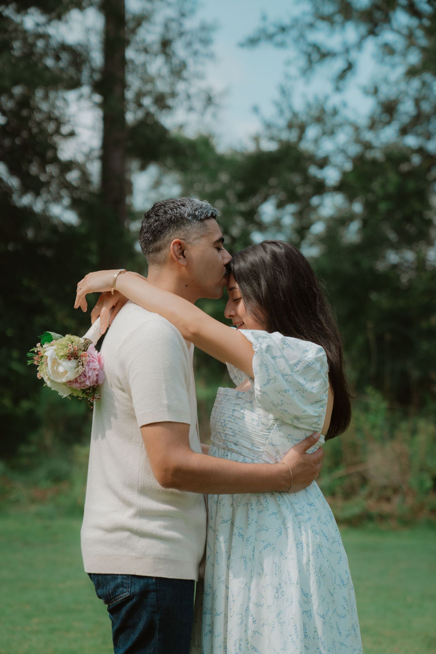 A romantic outdoor photoshoot with a couple embracing in a lush green garden setting.
