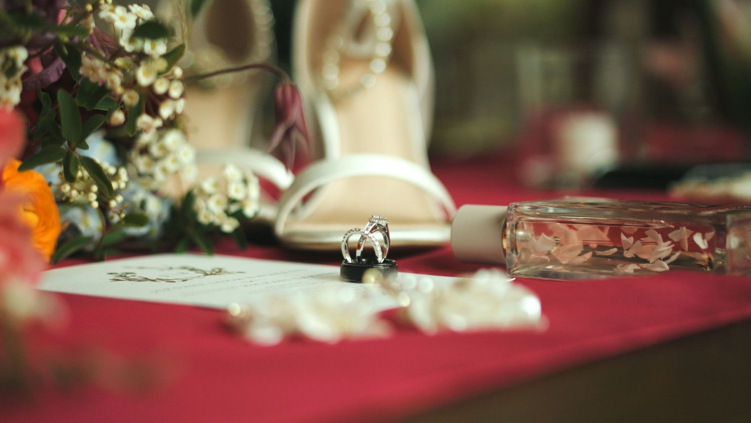 Wedding rings and details arranged on red tablecloth with shallow depth of field.