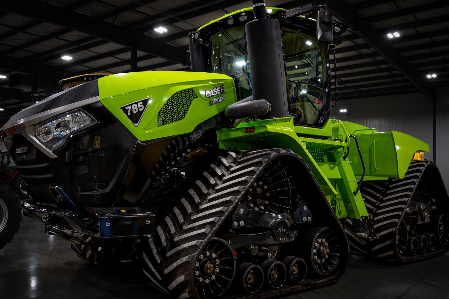 Modern green tractors and agricultural equipment displayed in dark showroom setting. Case IH Steiger 785