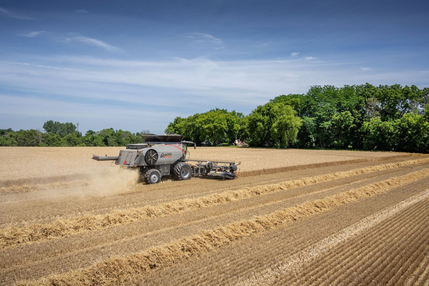 Tractor tilling rows in a dry agricultural field under bright blue skies.