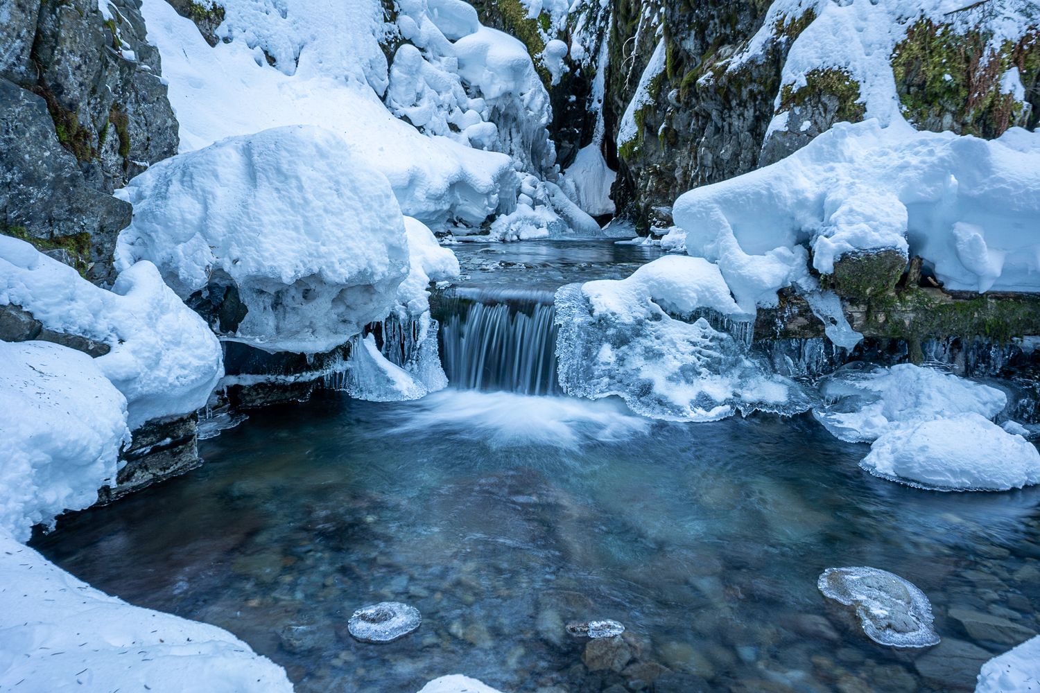 Frozen winter stream with icy formations and snow-covered rocks creating a serene winter landscape. Virgin Creek Falls Girdwood Alaska.