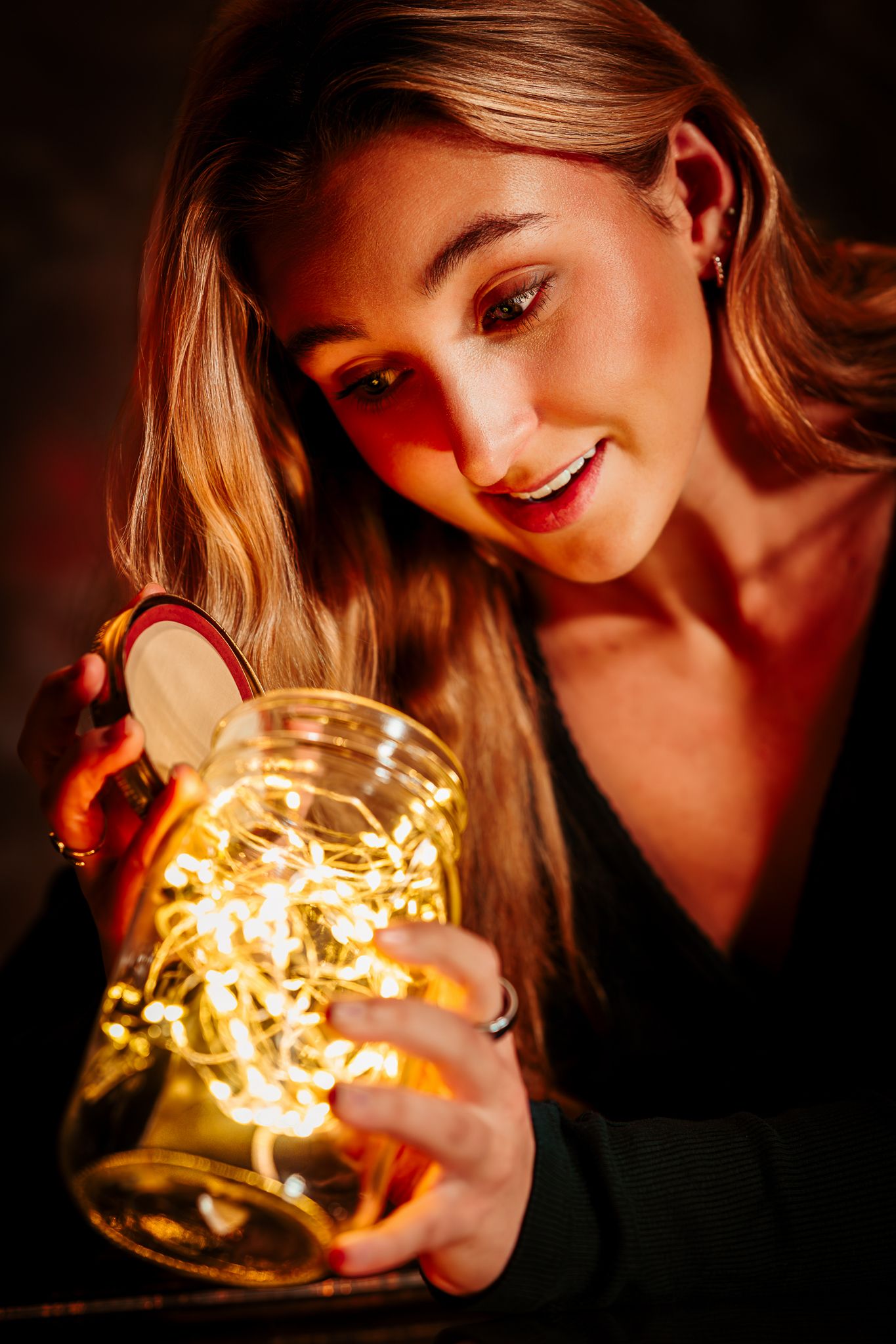 A young blonde woman smiling while holding a mason jar with fairy lights.