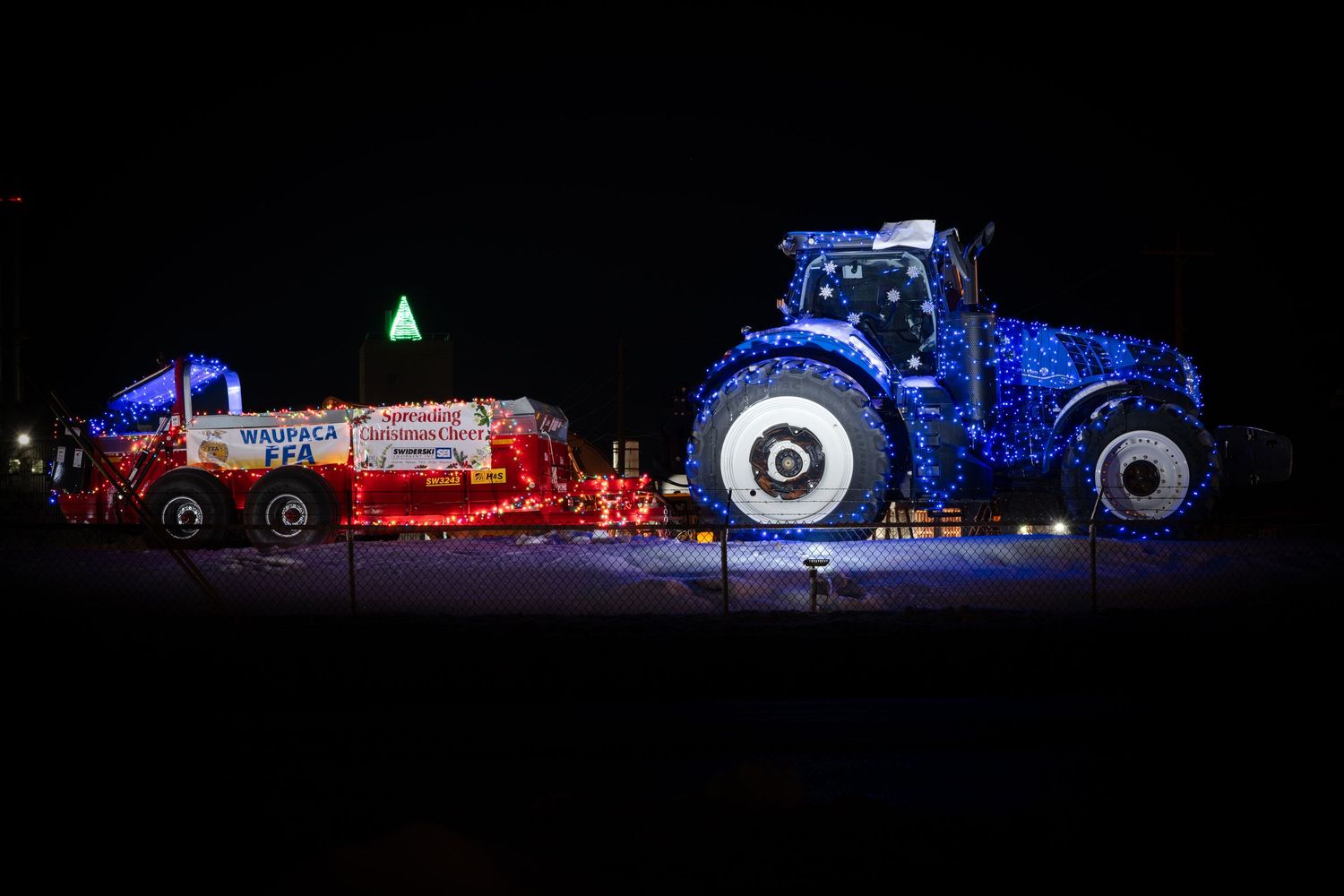 Illuminated farm equipment creates a dramatic light display against the dark night sky. New Holland t8.350.