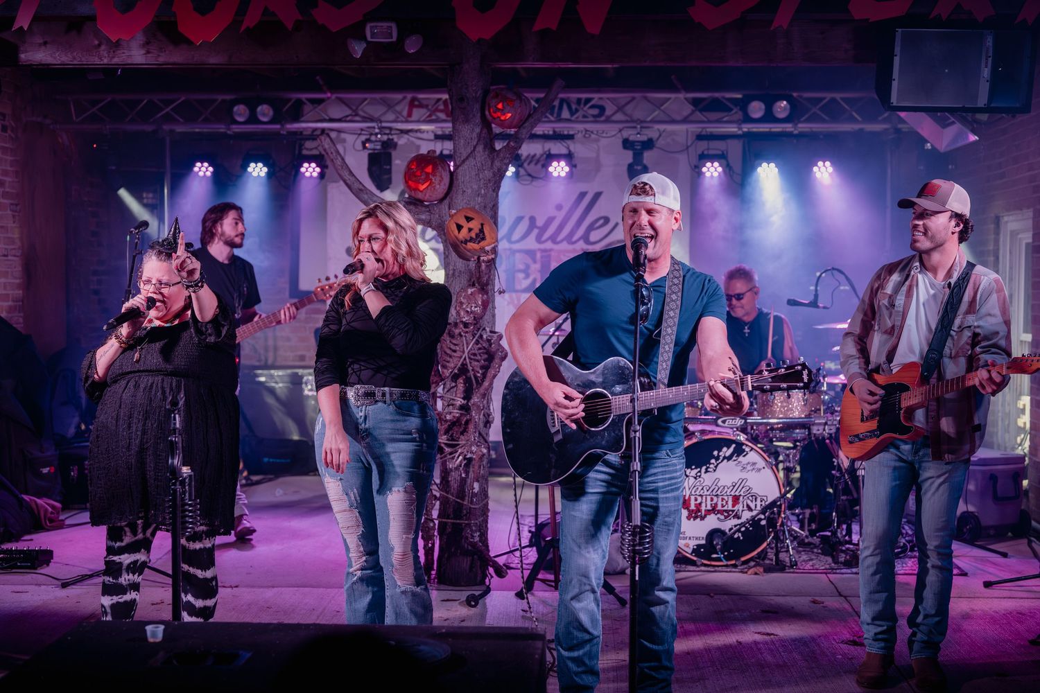 A live band performs on stage with colorful purple lighting at a music venue during an energetic concert performance. Nashville Pipeline