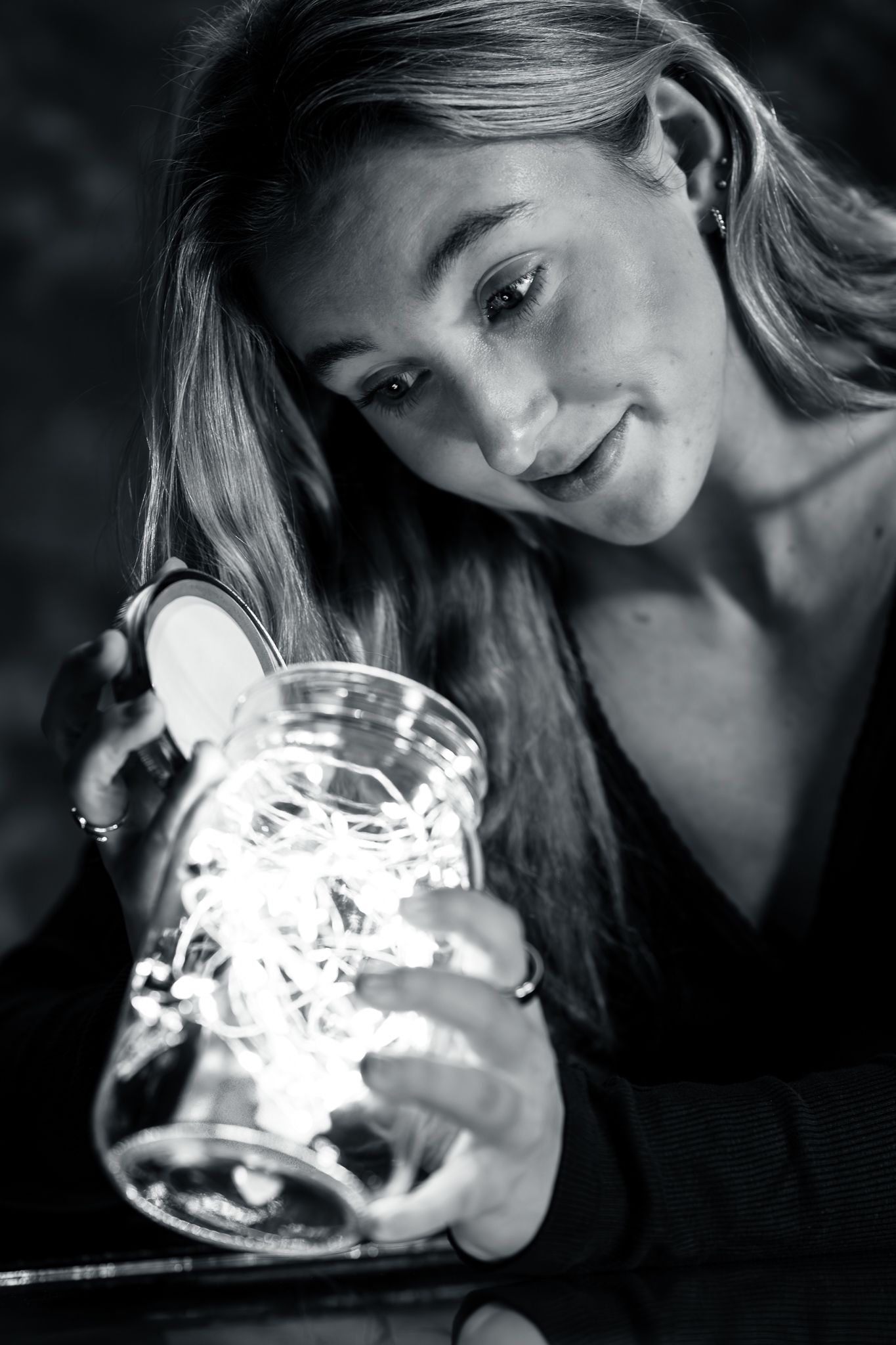 Young woman smiles while holding a mason jar filled with fairy lights in black and white portrait photo.