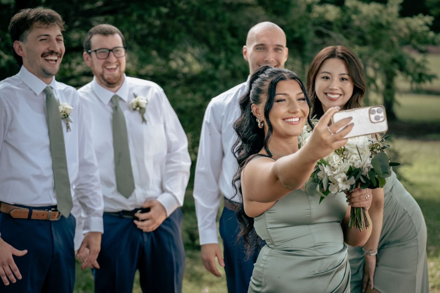 A bridesmaid takes a selfie with the wedding party outdoors during a celebration.