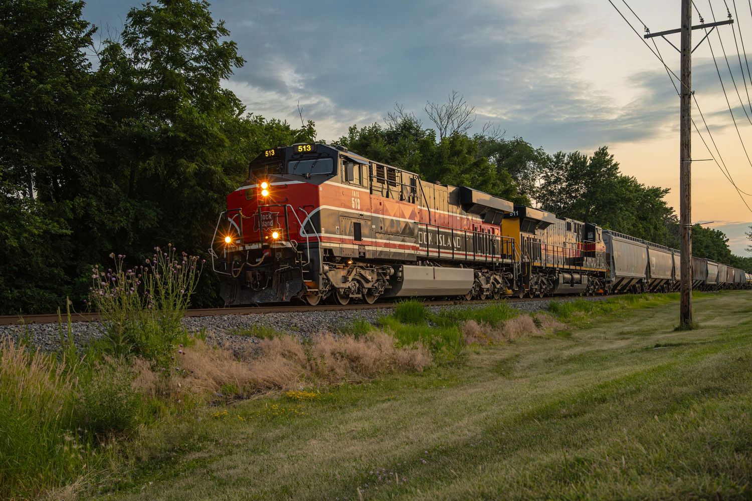 Freight trains passing through rural countryside at sunset with dramatic clouds.