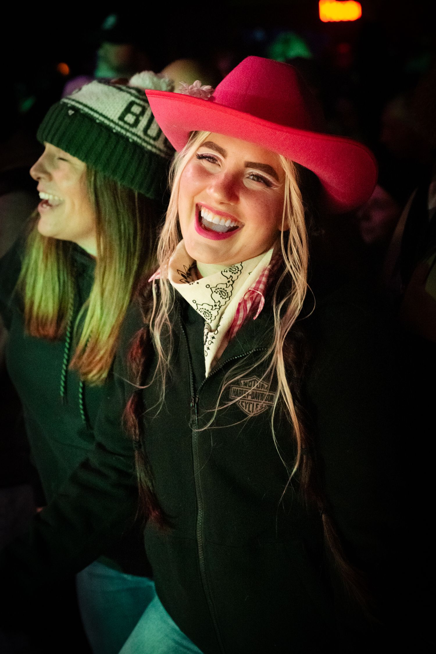Concert attendees wearing colorful caps and winter clothing illuminated by stage lighting.