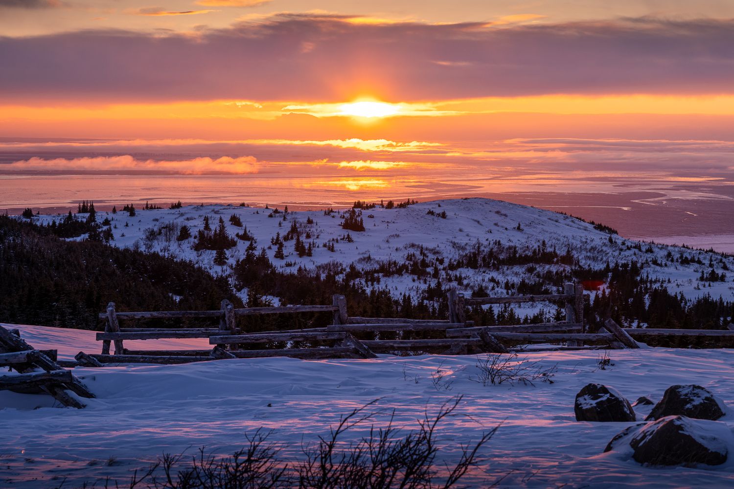 Stunning winter sunset over snow-covered mountains with orange sky and silhouetted landscape. Glen Alps Overlook Anchorage Alaska.