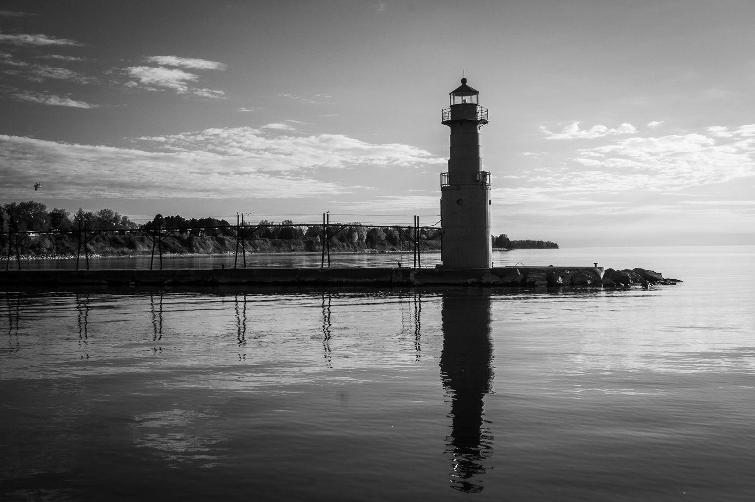 Black and white panorama of a lighthouse silhouetted against a calm water horizon at dusk.