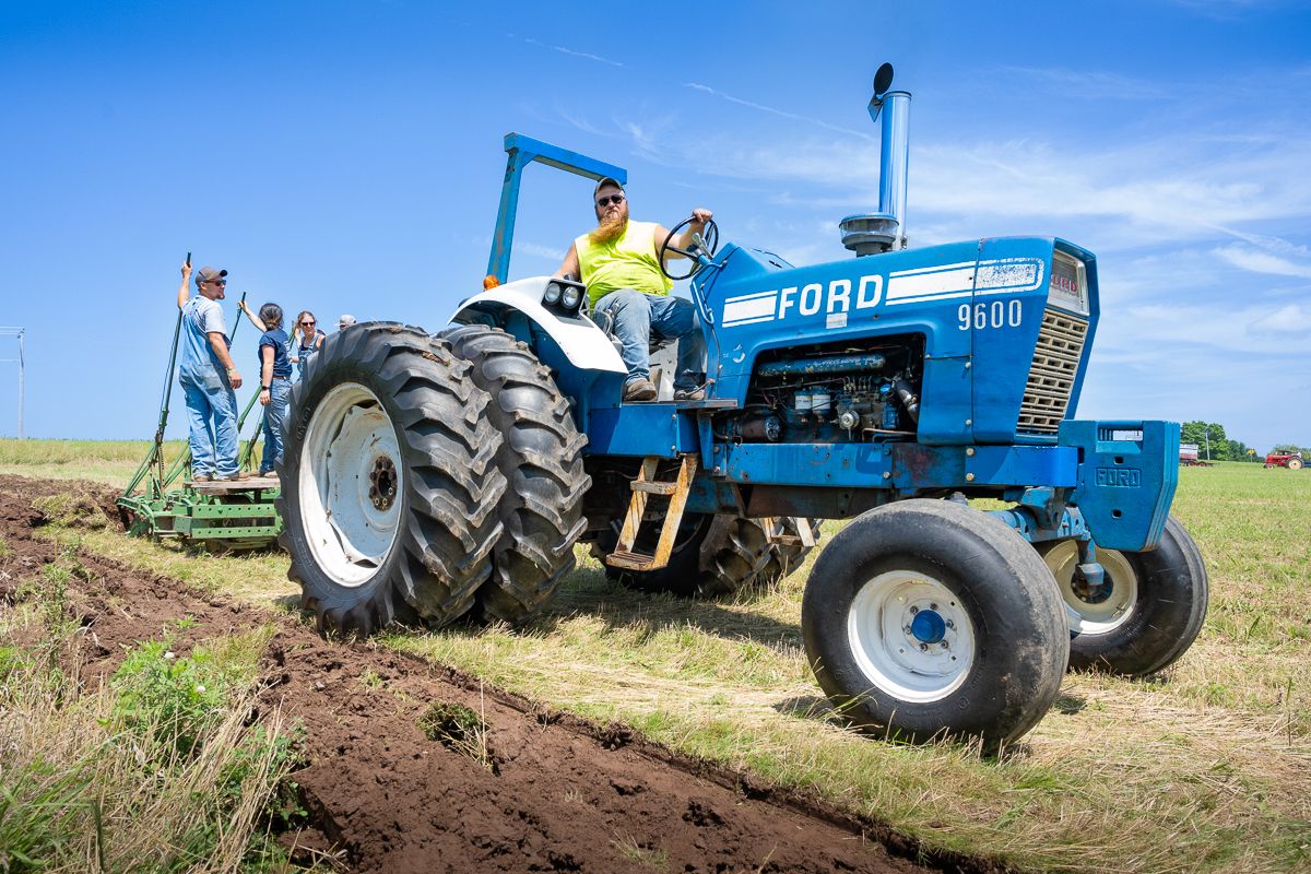 Blue tractors working in sequence across agricultural field under sunny sky. Ford 9600 plowing.