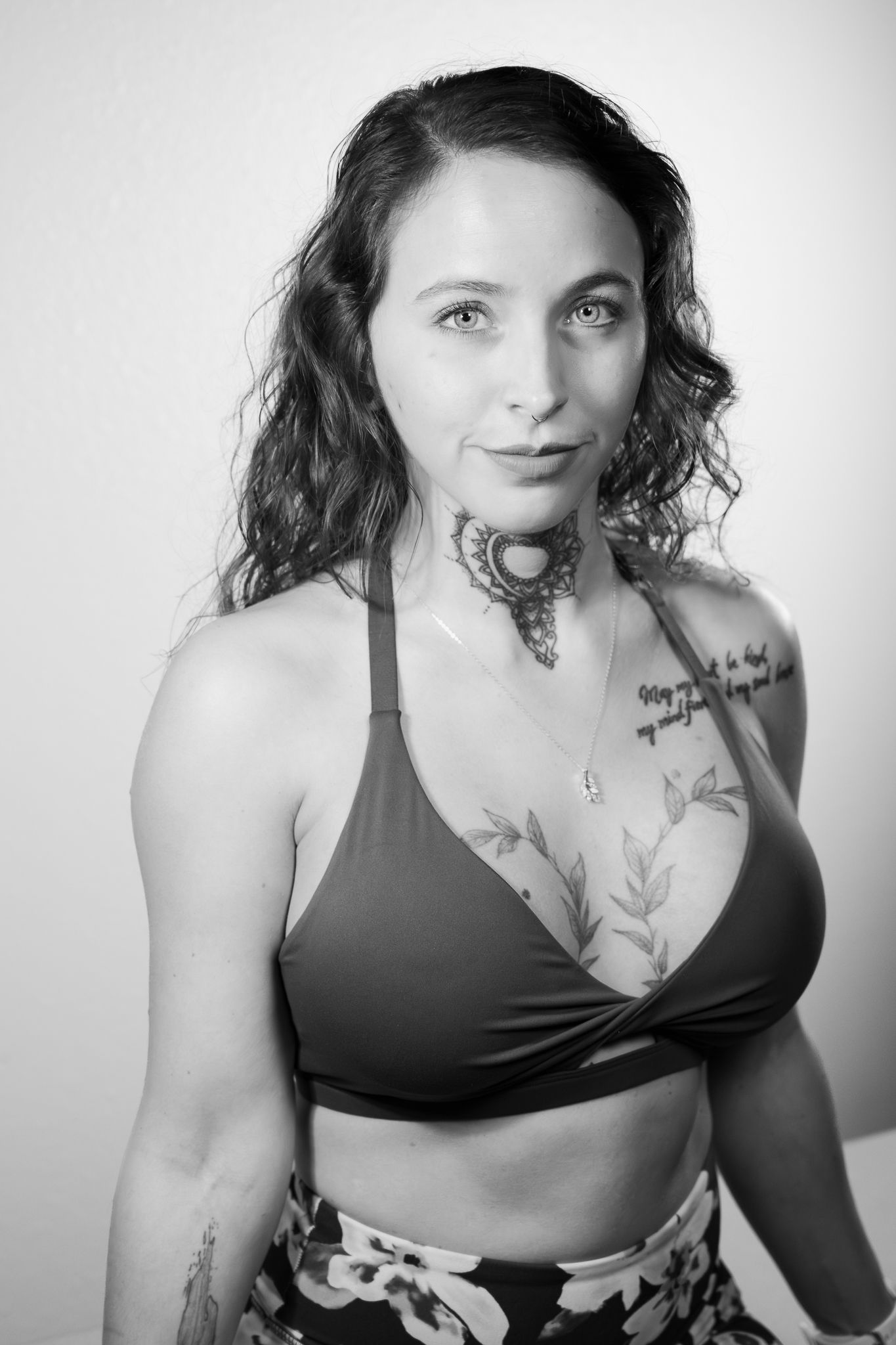 Black and white portrait of a tattooed woman in a bikini top posing confidently.