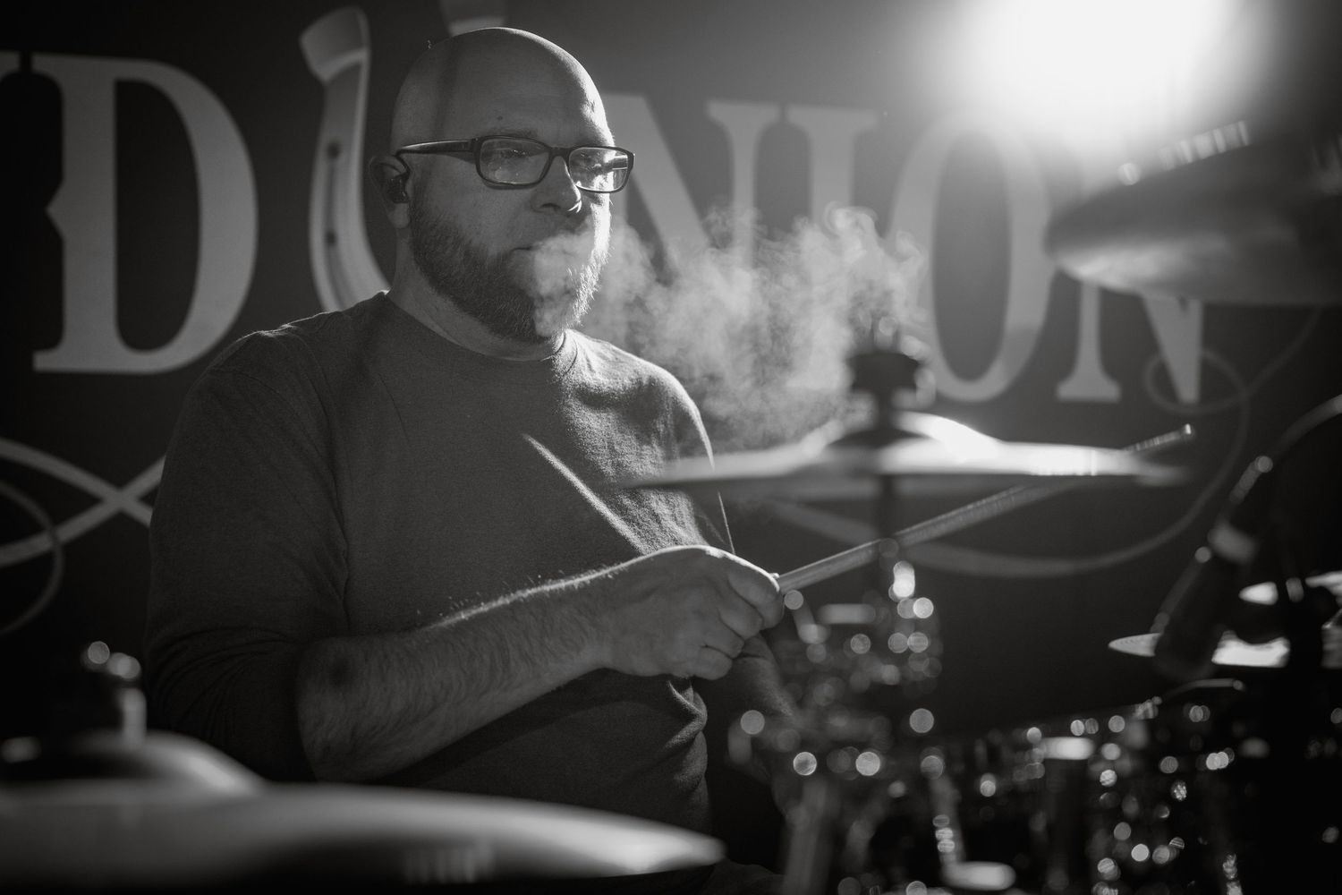 Black and white portrait of musician performing at a dimly lit venue with smoke effects. Grand Union.