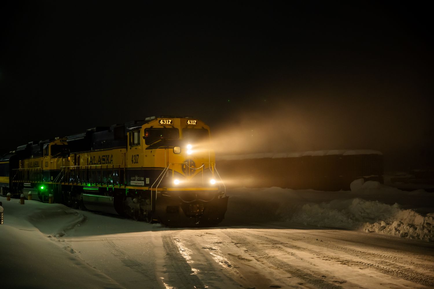 Illuminated train moving through snowy terrain at night with bright headlights. Alaska Railroad at Anchorage Alaska depot.