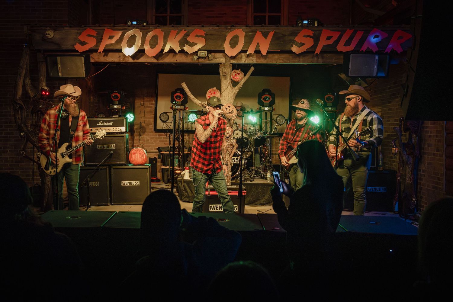 Wide shot of band performing on illuminated stage with vintage-style signage above. Avenue 55 Spooks on Spurr